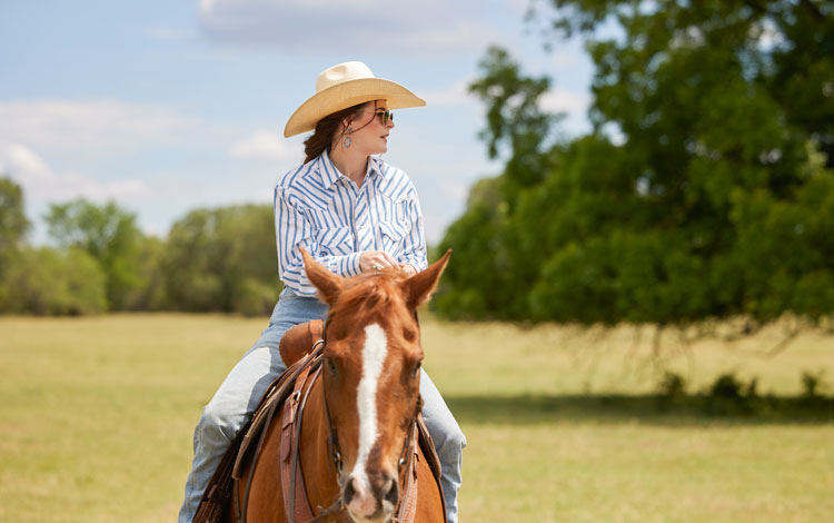 A cowgirl on her horse in an open field on a sunny day.